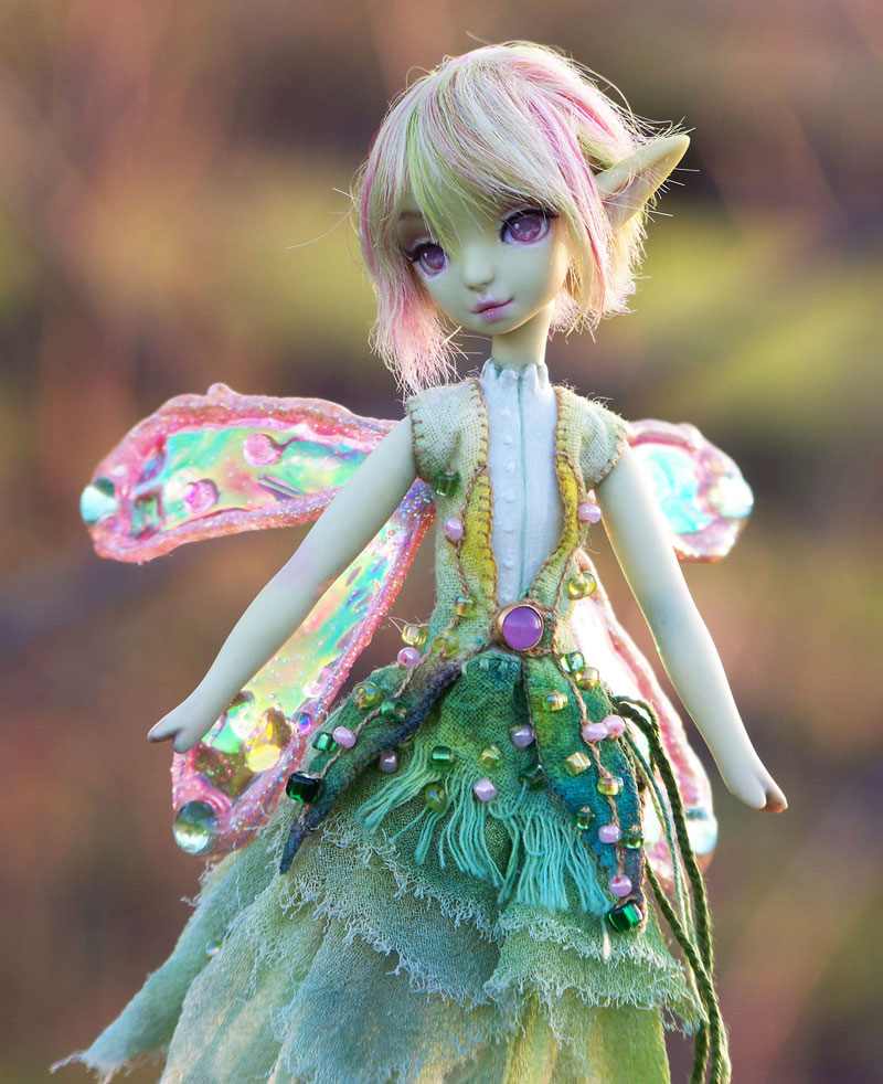 Close up of the dolls face, she has pink wings and purple eyes.