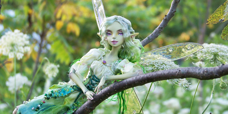 Green fairy porcelain bjd relaxing in a tree in a wildflower field.
